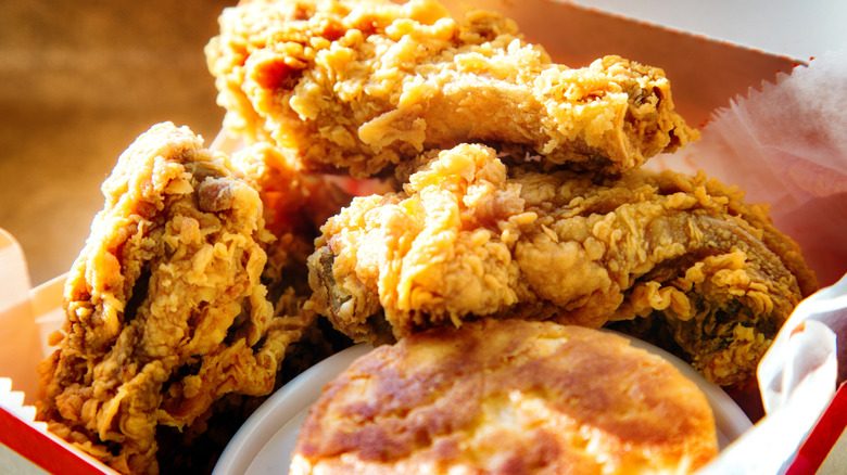 A fast-food basket with three pieces of fried chicken and a biscuit.