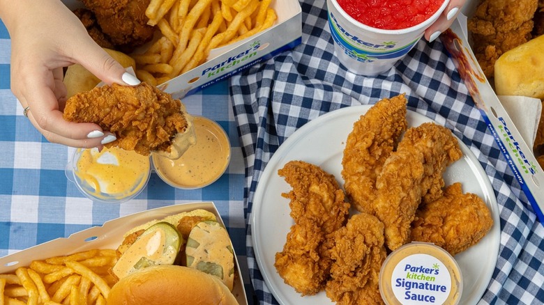 A spread of Parker's Kitchen food, including fried chicken, French fries, a chicken sandwich, sauces, and a drink.