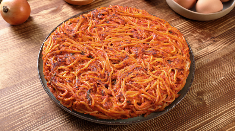 Spaghetti in red sauce omelet on plate next to eggs, onions, spices