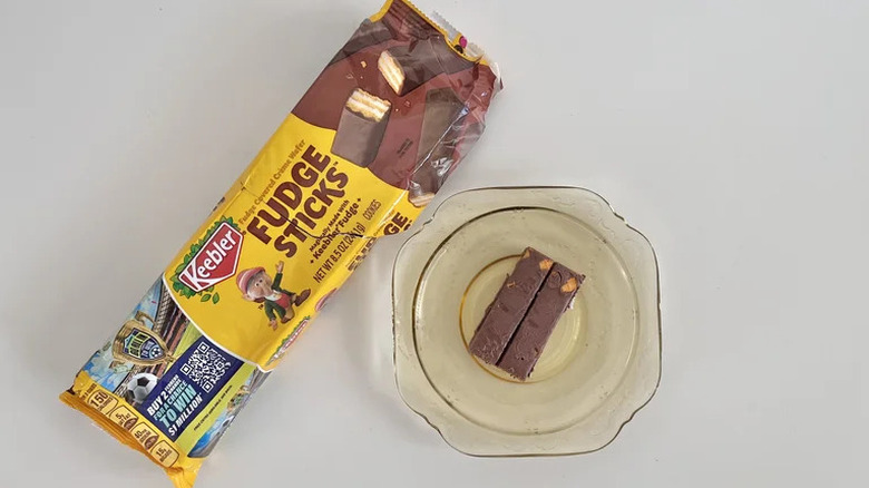 A packet of Keebler Fudge Sticks Original next to two of the cookies on a plate on a white table