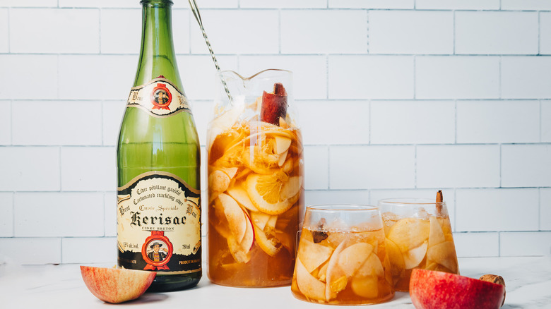Pitcher and two glasses of of apple sangria beside ingredients