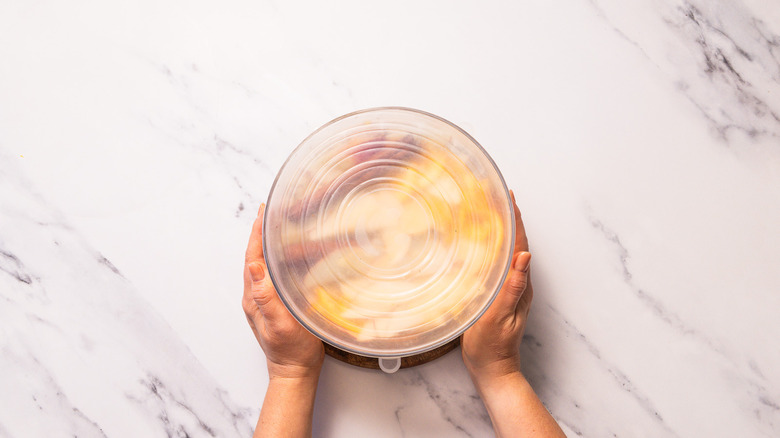 Hands holding a glass bowl topped with silicone cover