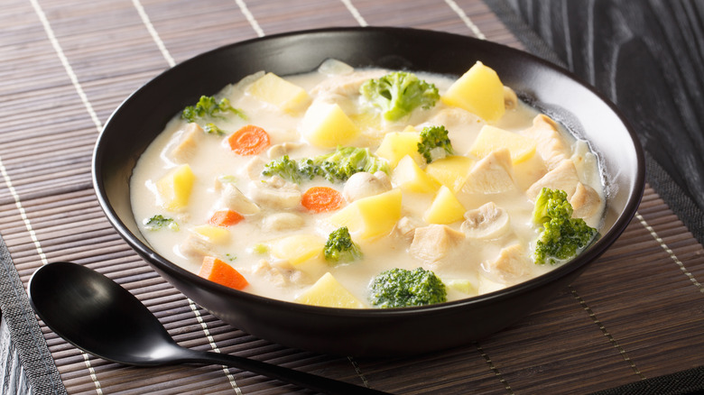 a black bowl full of roux-thickened soup with chicken, potatoes, carrots, and broccoli