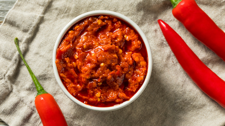 Dish of crushed Calabrian chile sauce surrounded by whole peppers