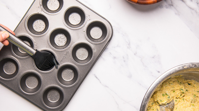 Brushing muffin tins with oil.