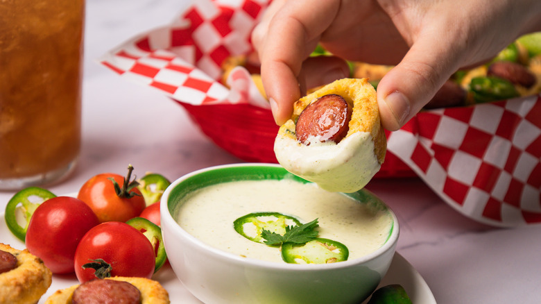 Close up on dipping a corn dog into spicy jalapeno crema.
