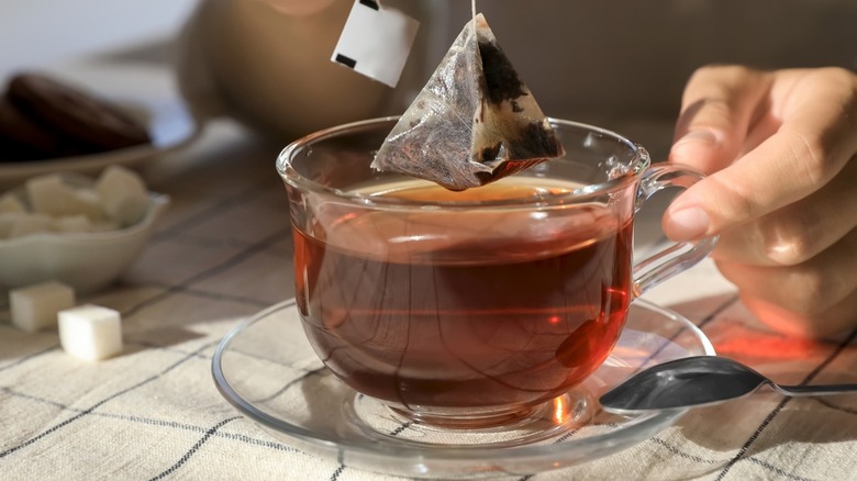 Hand dipping a tea bag into a glass mug of black tea