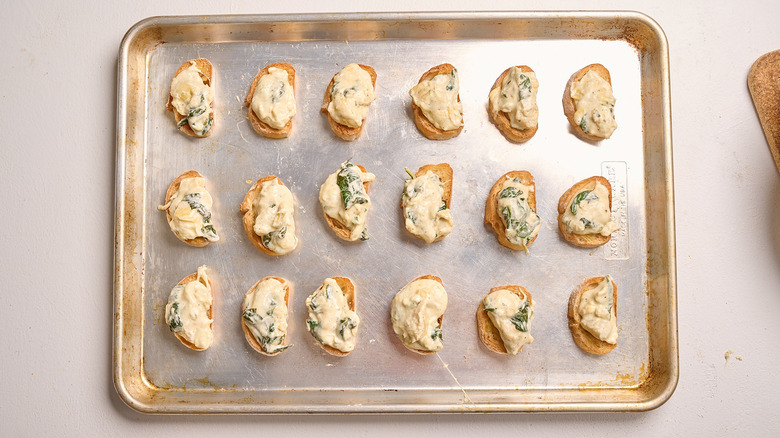 spreading spinach and artichoke dip onto crostini