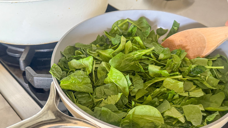 wooden spoon stirring spinach in pan