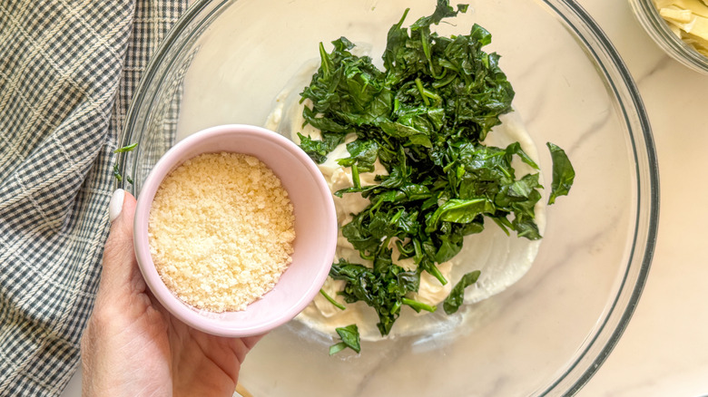 hand adding cheese to bowl with spinach