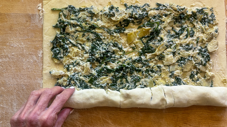 Hands rolling spinach artichoke pastry sheet