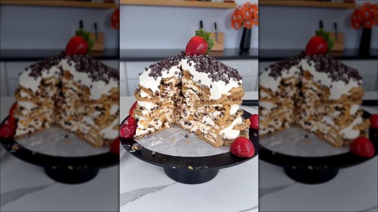 A multi-layered chocolate chip cookie icebox cake garnished with whipped cream, mini chocolate chips, and strawberries