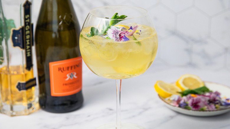 Springtime Hugo Spritz with mint, edible flowers and lemon slice and all components in background