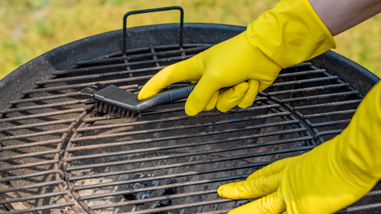 Someone cleaning a grill with a brush and rubber gloves