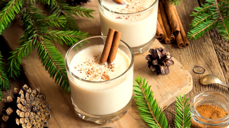 Glasses of eggnog with cinnamon sticks, pine cones