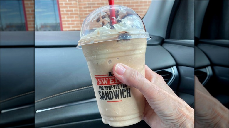 Hand holding an Arby's Jamocha Shake with whipped cream and chocolate sauce