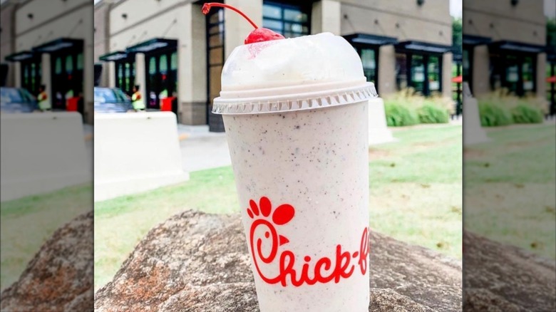 Chick-fil-A Cookies & Cream Milkshake topped with a cherry in front of restaurant location