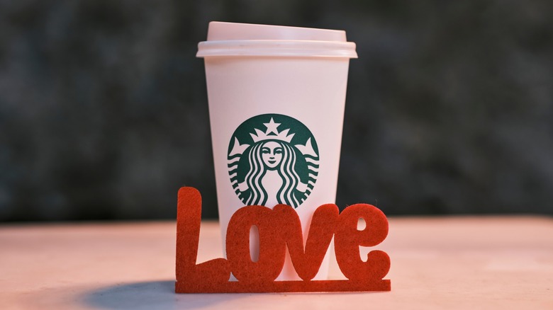A Starbucks branded hot cup with a letter sign that says "Love"
