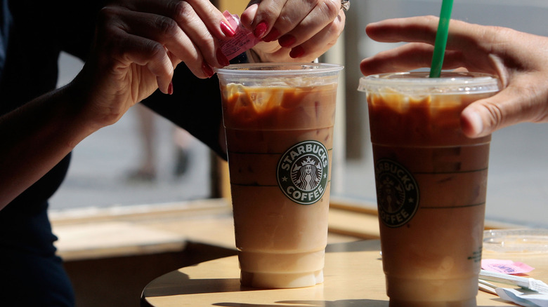 hands adding sugar to iced coffee drink