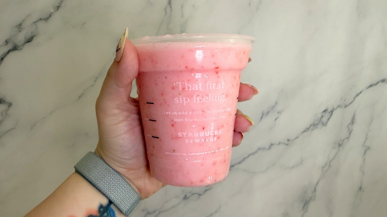 Hand holding Starbucks Pink Drink on marble background