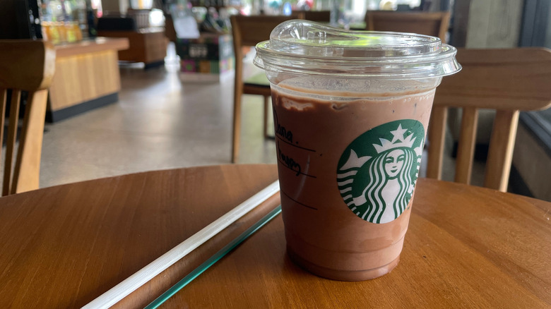 A cup of Starbucks chocolate milk on a table next to a straw