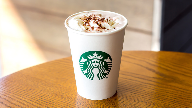 A Starbucks hot chocolate in a cup with whipped cream and cocoa powder on a table