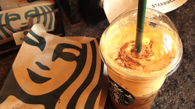 Starbucks paper food bag next to cup of iced pumpkin drink with green straw