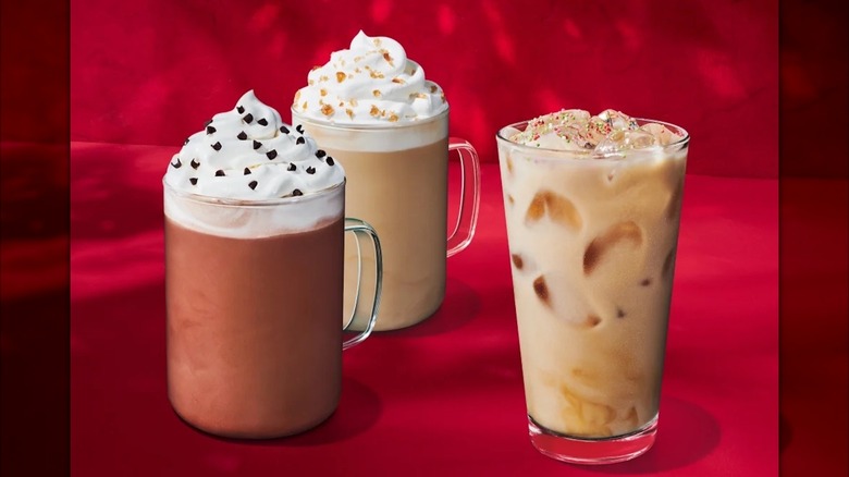 A selection of drinks and snacks on the new Starbucks holiday menu including ice drinks, whipped cream top beverages, cookies and pastries on a red background