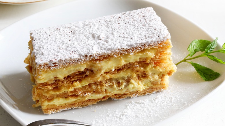 A plated mille-feuille dessert dusted with powdered sugar and garnished with a mint sprig
