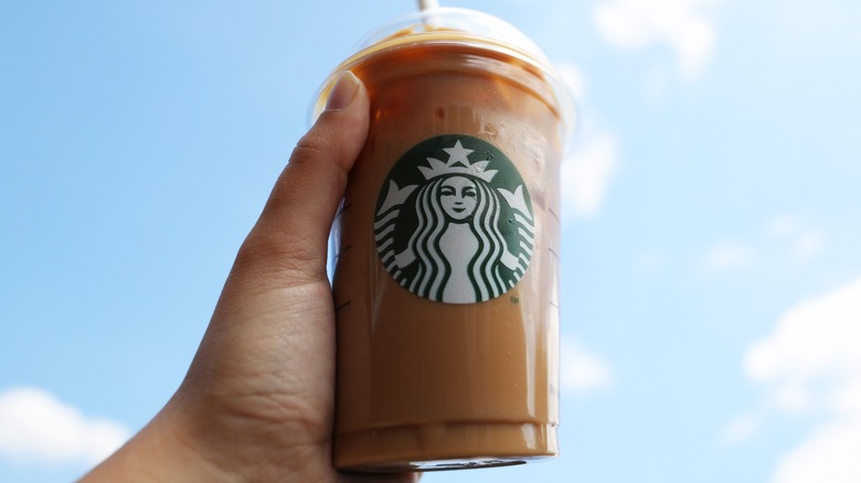 Hand holding an iced Starbucks drink with a blue sky background