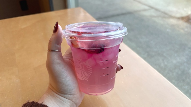 Hand holding Starbucks Pink Cannon Ball Drink over table in cafe