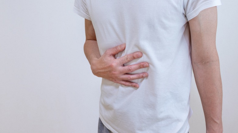 A man and a white shirt viewed from the chest down holding his own abdomen