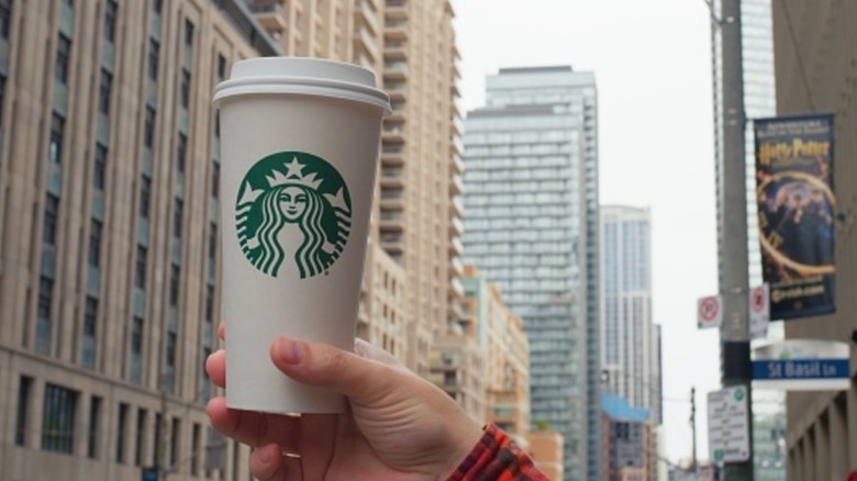A hand holding a Starbucks cup in front of a cityscape