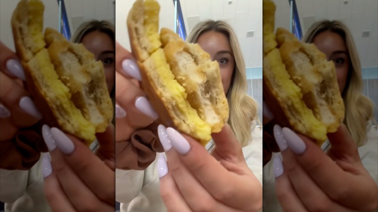 Mirrored image of woman holding half eaten sandwich to camera