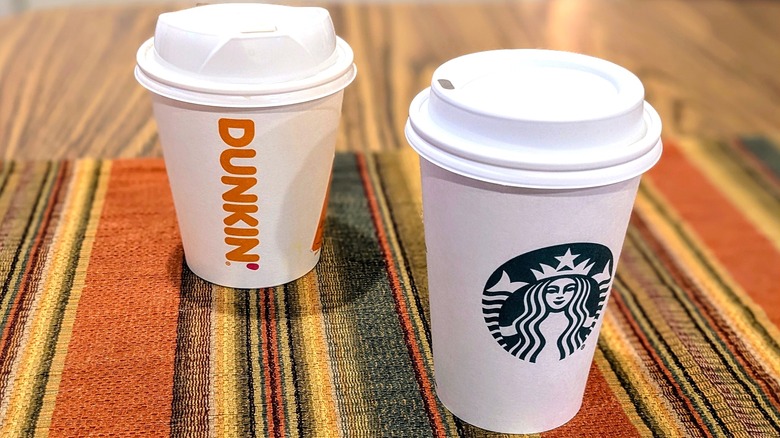 A small Dunkin' paper cup and a small Starbucks paper cup on striped linen