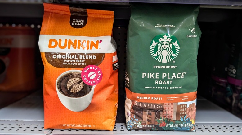 A bag of Dunkin' coffee beans and a bag of Starbcuks' beans on a shelf at the store