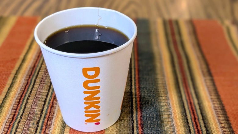 A small paper cup of Dunkin black coffee with no lid on striped linen