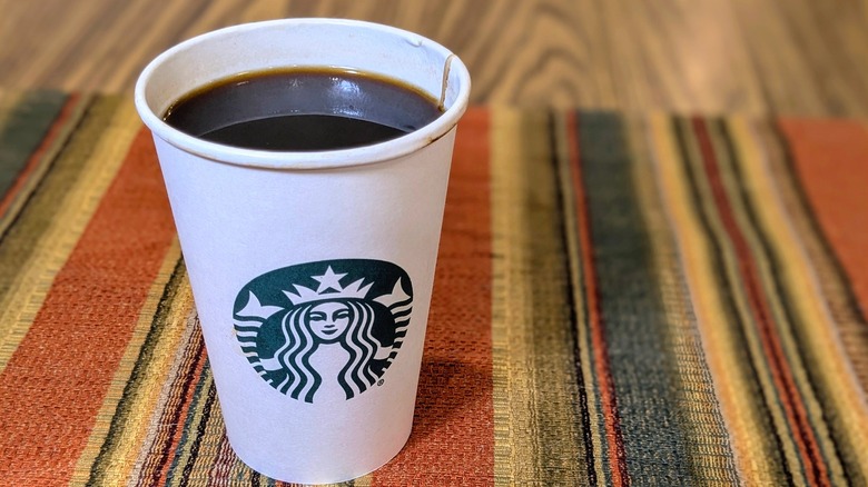 A paper Starbucks cup of black coffee with no lid on striped linen
