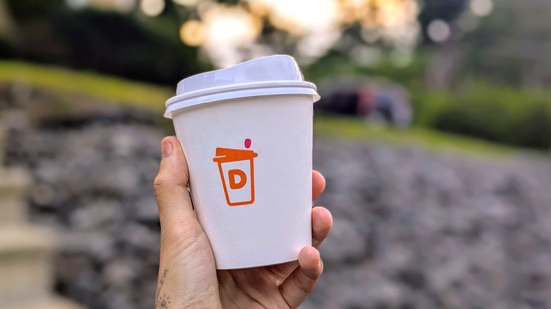 A hand holds a Dunkin' cup outside at sunset