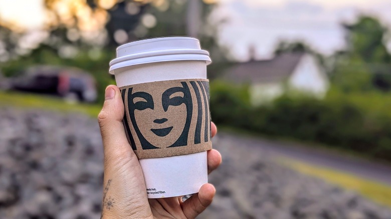 A hand holds a Starbucks paper cup outside at sunset