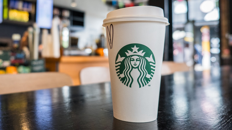 A Styrofoam Starbucks cup sitting on a countertop inside a Starbucks location