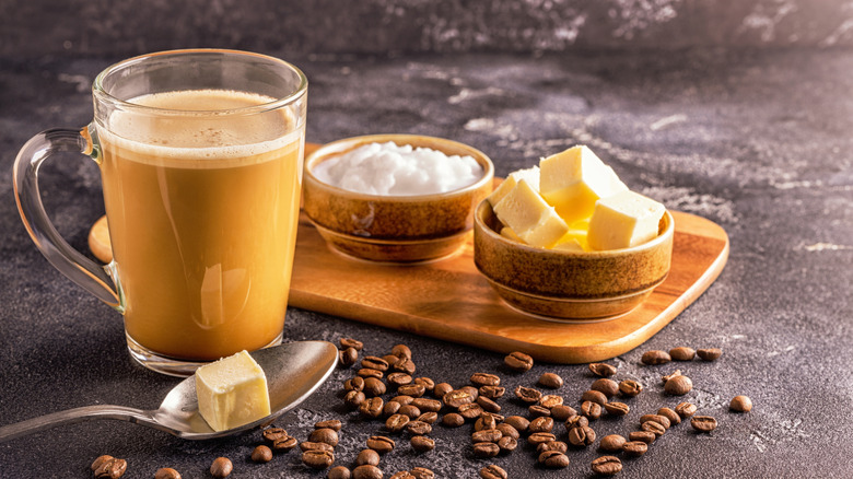 A mug of creamy coffee with butter, sugar, coffee beans and a spoon
