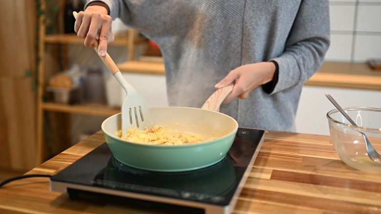 A persons scrambling eggs in blue pan