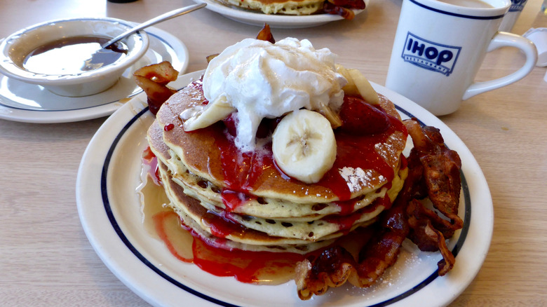 IHOP pancakes topped with fruit and sauces syrup, served with bacon and side of coffee
