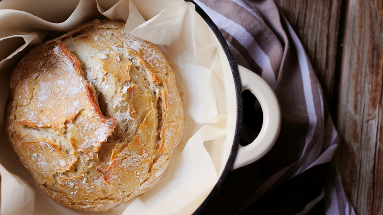 White dutch oven with baked bread inside on wood table