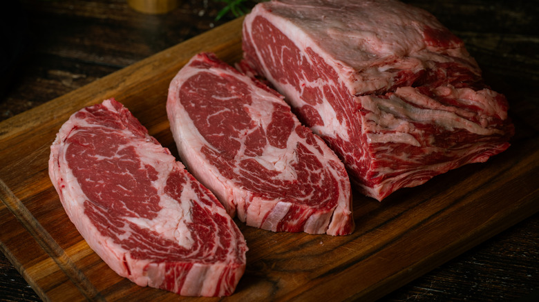 A ribeye being sliced into chunks on a wooden cutting board