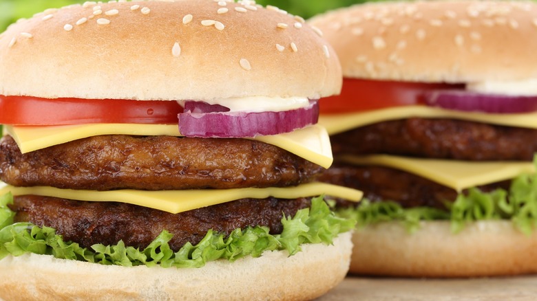 Two double cheeseburgers sit on a wooden counter in front of a green backdrop