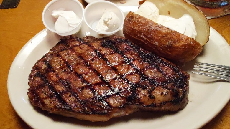 Grilled ribeye steak from Texas Roadhouse on white plate next to baked potato with whipped butter