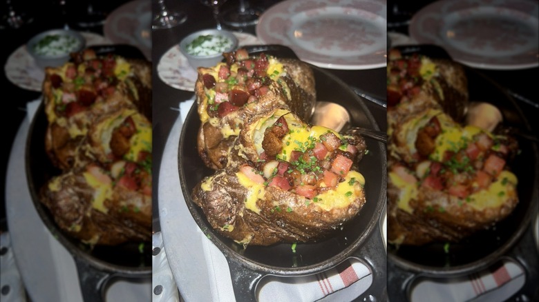 Baked potatoes in black baking dish, each loaded with cheese, bacon, and chives
