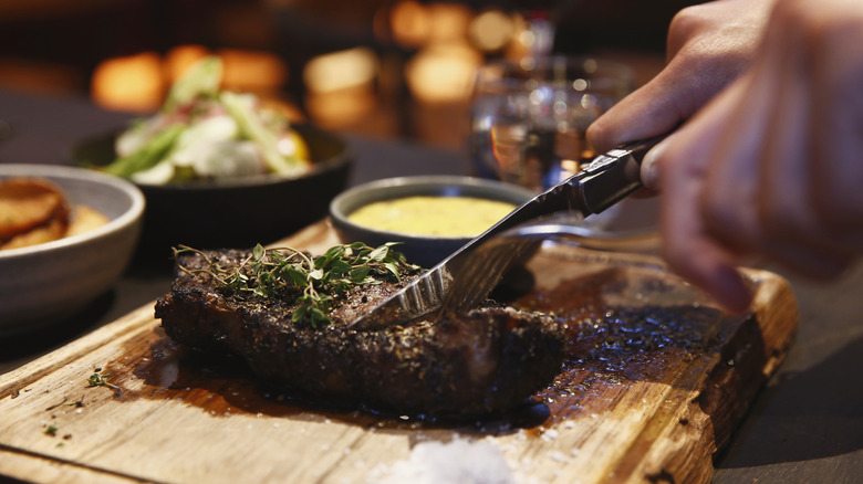 Hands cutting steak with knife and fork in restaurant setting